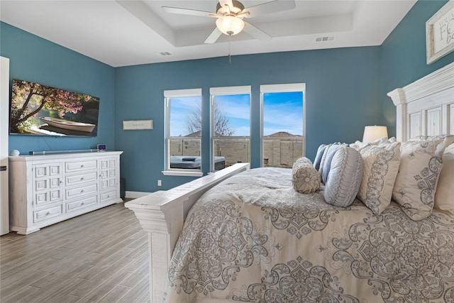 bedroom with hardwood / wood-style flooring, ceiling fan, and a tray ceiling