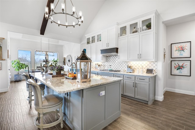 kitchen with a kitchen island with sink, pendant lighting, stainless steel gas cooktop, and decorative backsplash