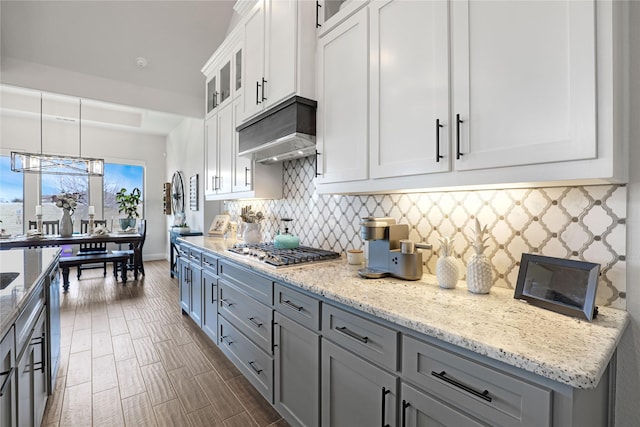 kitchen with appliances with stainless steel finishes, white cabinetry, hanging light fixtures, light stone countertops, and decorative backsplash