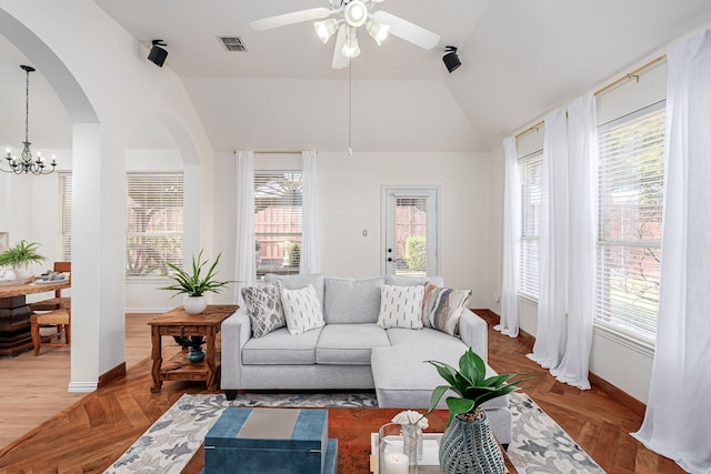 living room with a healthy amount of sunlight, ceiling fan with notable chandelier, vaulted ceiling, and parquet flooring