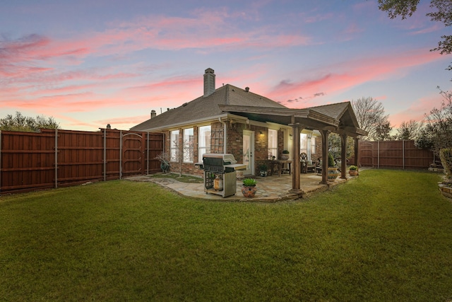 back house at dusk with a patio area and a lawn