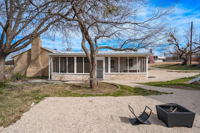 rear view of property featuring a fire pit and a sunroom