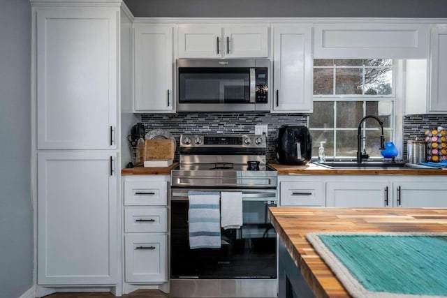 kitchen with wood counters, stacked washer / drying machine, white cabinets, and appliances with stainless steel finishes