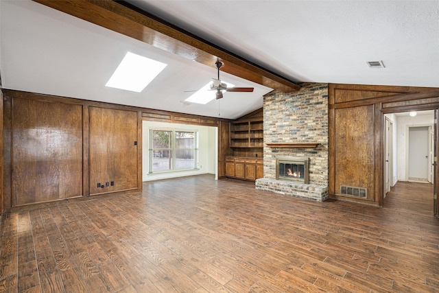 unfurnished living room with a brick fireplace, dark wood-type flooring, lofted ceiling with skylight, and wooden walls