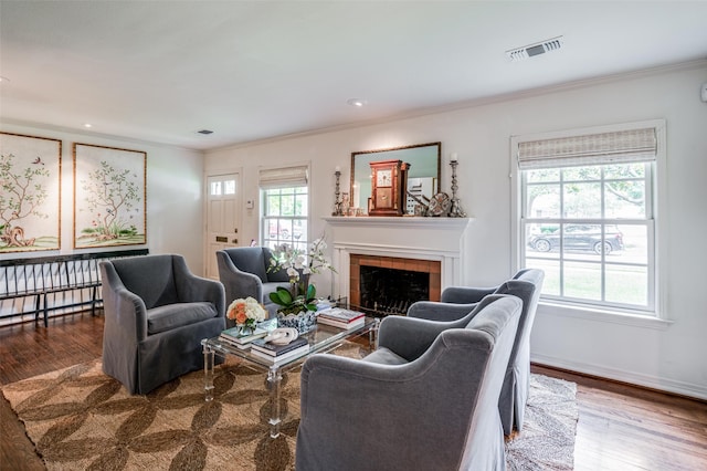 living room with hardwood / wood-style flooring, a tile fireplace, ornamental molding, and a wealth of natural light