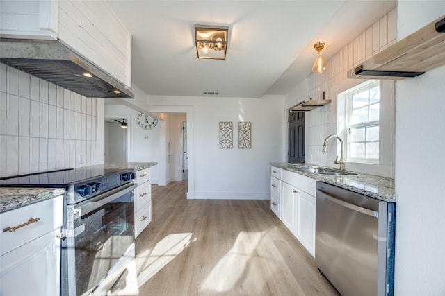 kitchen with wall chimney exhaust hood, sink, white cabinets, light stone counters, and stainless steel appliances