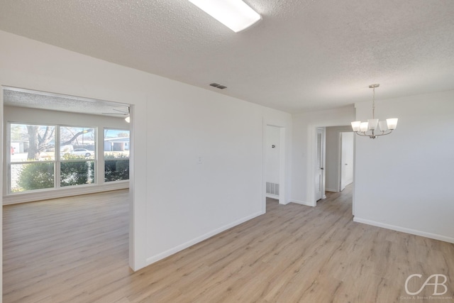 empty room featuring an inviting chandelier, light hardwood / wood-style floors, and a textured ceiling