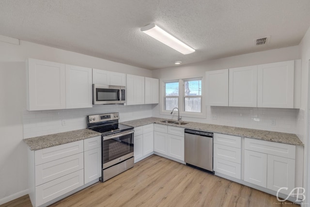 kitchen featuring sink, light hardwood / wood-style flooring, appliances with stainless steel finishes, white cabinetry, and a textured ceiling