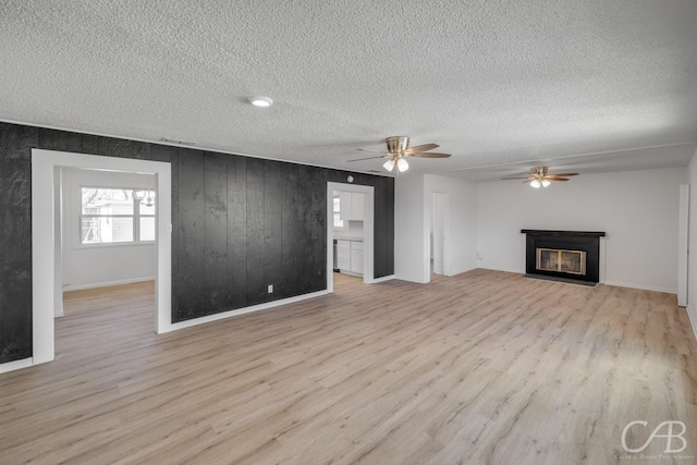 unfurnished living room featuring wood walls, light wood-type flooring, a textured ceiling, and ceiling fan