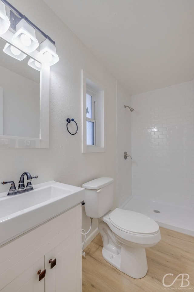 bathroom featuring a tile shower, vanity, wood-type flooring, and toilet