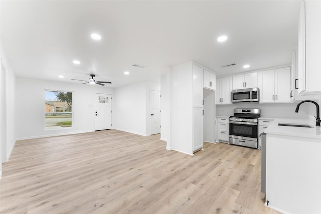 kitchen featuring light countertops, appliances with stainless steel finishes, open floor plan, white cabinetry, and a sink