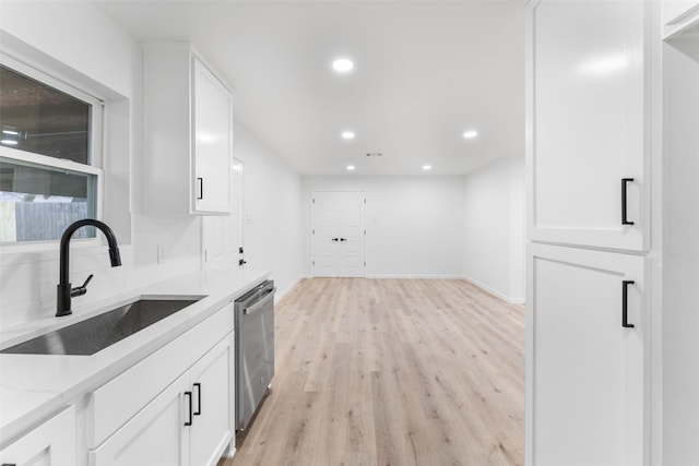 kitchen with white cabinets, sink, light stone counters, stainless steel dishwasher, and light hardwood / wood-style flooring