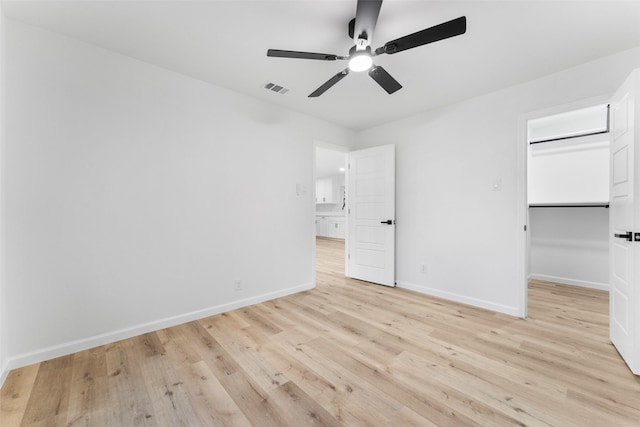 unfurnished bedroom featuring light wood-type flooring, a walk in closet, visible vents, and baseboards