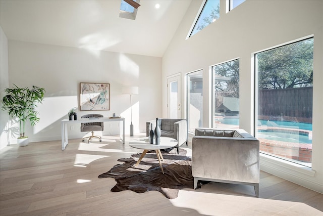 sitting room with a wealth of natural light, a skylight, high vaulted ceiling, and light wood-type flooring