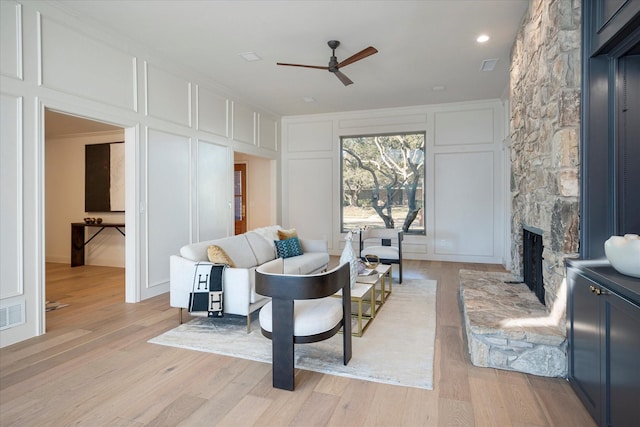 living room with ceiling fan, a fireplace, and light hardwood / wood-style floors