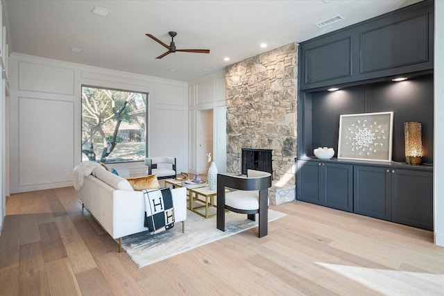 living room featuring ceiling fan, a stone fireplace, and light hardwood / wood-style floors