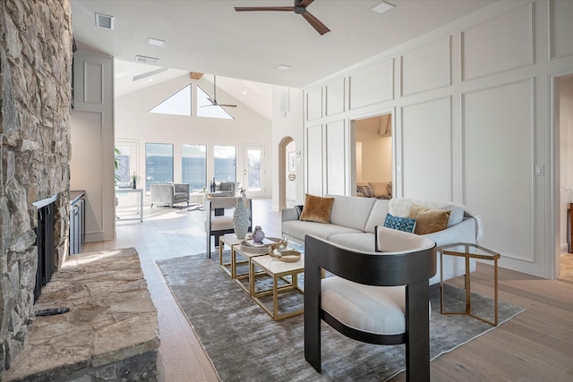 living room with ceiling fan, high vaulted ceiling, a fireplace, and light hardwood / wood-style flooring