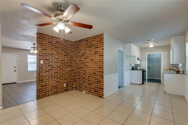 tiled spare room featuring ceiling fan, sink, brick wall, and a textured ceiling