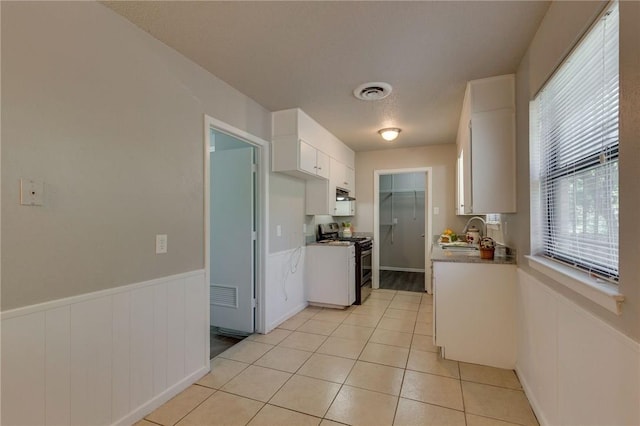 kitchen with light tile patterned floors, sink, white cabinets, and stainless steel gas range oven