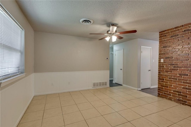 spare room with ceiling fan, brick wall, a textured ceiling, and light tile patterned flooring