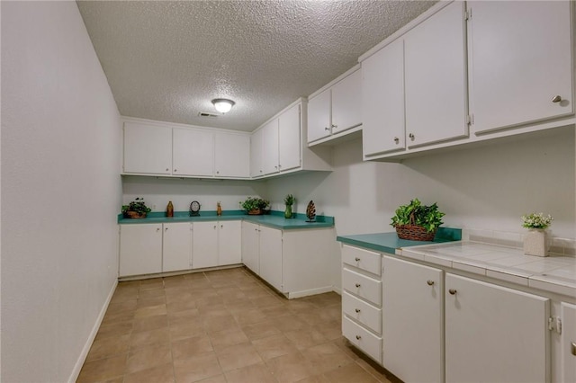 kitchen featuring white cabinets, a textured ceiling, and tile countertops