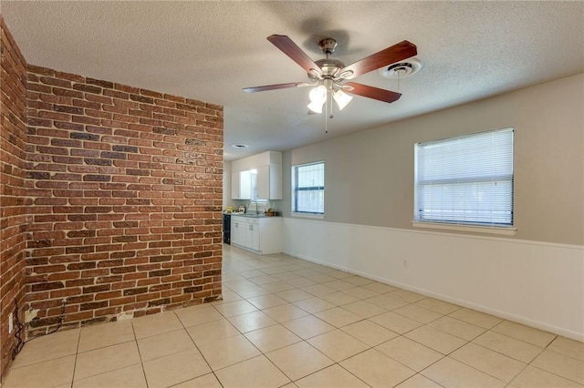 unfurnished room featuring sink, a textured ceiling, brick wall, and ceiling fan