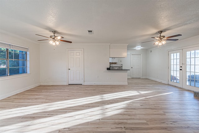 unfurnished living room with a textured ceiling, crown molding, french doors, and light wood-type flooring