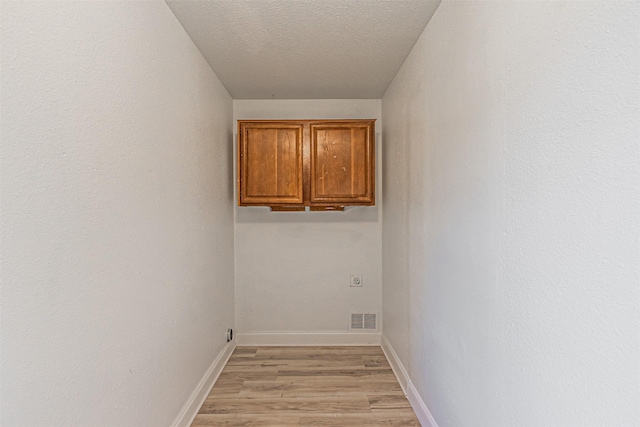 laundry room with a textured ceiling, light hardwood / wood-style floors, and cabinets