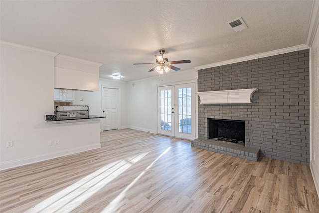 unfurnished living room with a textured ceiling, french doors, a brick fireplace, light hardwood / wood-style flooring, and crown molding