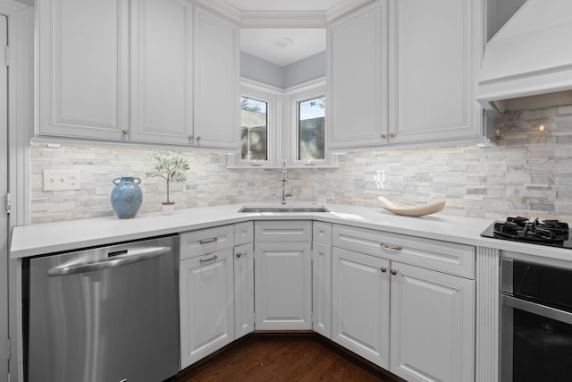 kitchen with appliances with stainless steel finishes, tasteful backsplash, custom range hood, sink, and white cabinets