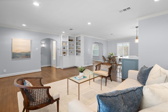 living room featuring built in shelves, light hardwood / wood-style flooring, and crown molding