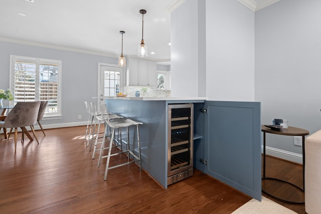 kitchen with kitchen peninsula, a kitchen breakfast bar, hanging light fixtures, ornamental molding, and beverage cooler