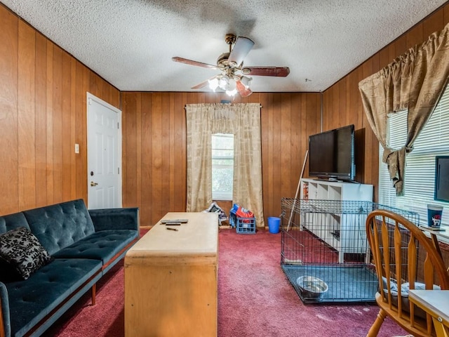 carpeted living room featuring ceiling fan, a textured ceiling, and wood walls