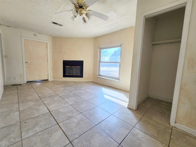 unfurnished living room featuring ceiling fan, light tile patterned floors, and a textured ceiling