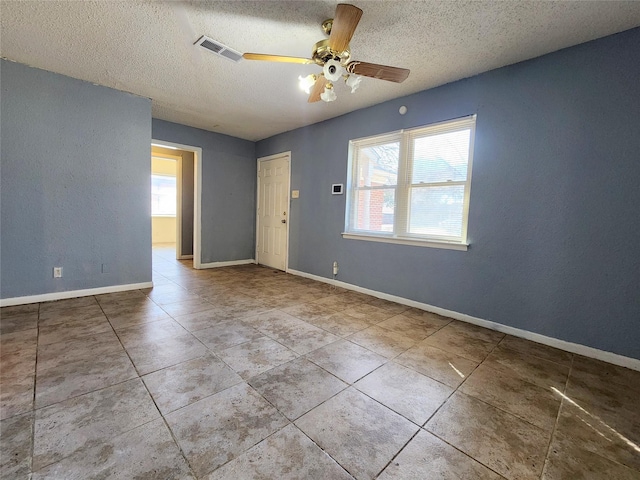 tiled empty room with ceiling fan, plenty of natural light, and a textured ceiling