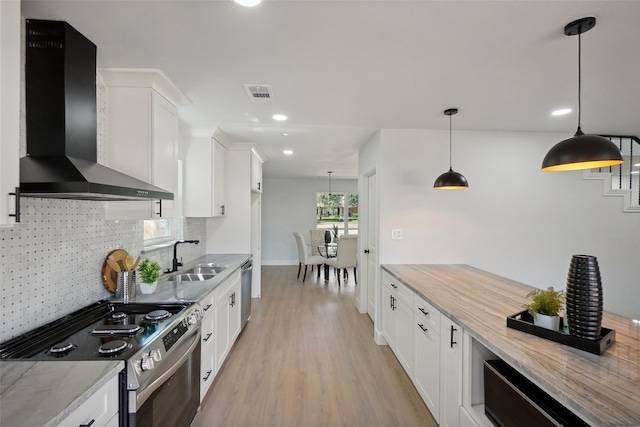 kitchen featuring appliances with stainless steel finishes, white cabinetry, sink, decorative light fixtures, and wall chimney exhaust hood