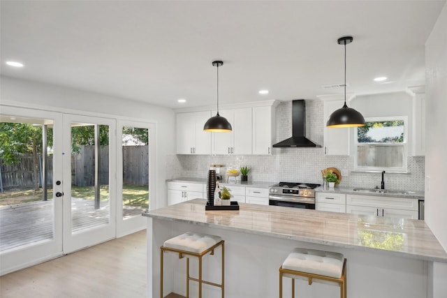 kitchen featuring white cabinets, stainless steel range, wall chimney range hood, tasteful backsplash, and sink