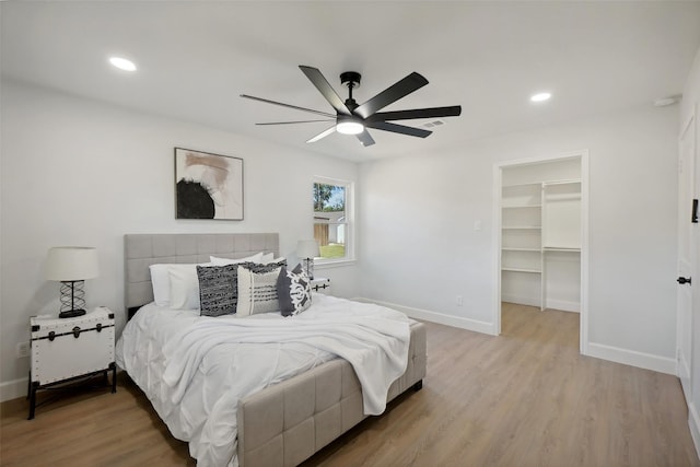 bedroom with light hardwood / wood-style floors, a closet, a spacious closet, and ceiling fan