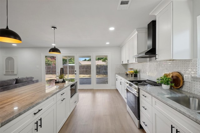 kitchen featuring pendant lighting, wall chimney range hood, white cabinetry, tasteful backsplash, and stainless steel gas stove