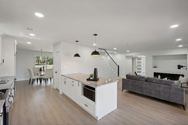 kitchen featuring hanging light fixtures, stainless steel stove, white cabinets, light stone counters, and light hardwood / wood-style floors