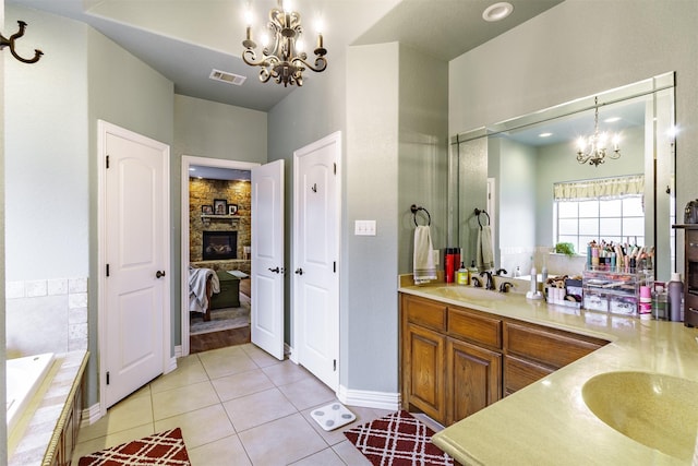 bathroom with tile patterned floors, vanity, a stone fireplace, and an inviting chandelier