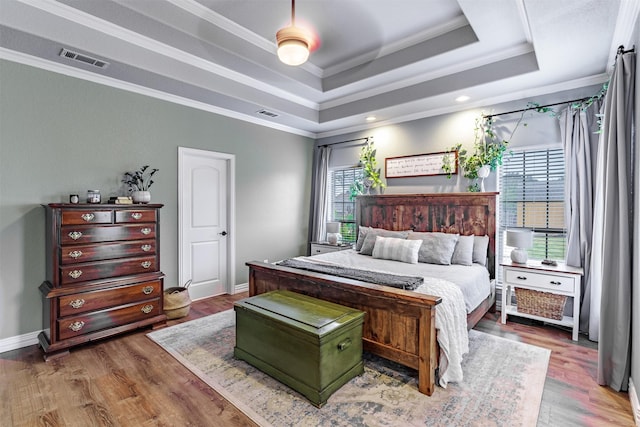 bedroom with hardwood / wood-style flooring, a raised ceiling, and crown molding