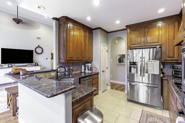 kitchen with appliances with stainless steel finishes, dark stone countertops, sink, kitchen peninsula, and a breakfast bar area