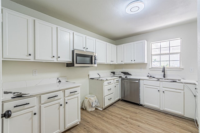 kitchen with light stone countertops, light hardwood / wood-style floors, white cabinetry, sink, and stainless steel appliances