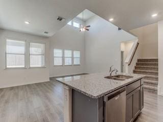 kitchen featuring sink, dishwasher, a kitchen island with sink, light stone countertops, and light hardwood / wood-style floors