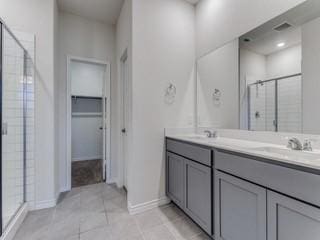 bathroom with double vanity, a stall shower, a spacious closet, and a sink