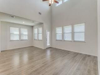 unfurnished living room featuring visible vents, ceiling fan, a towering ceiling, and light wood finished floors