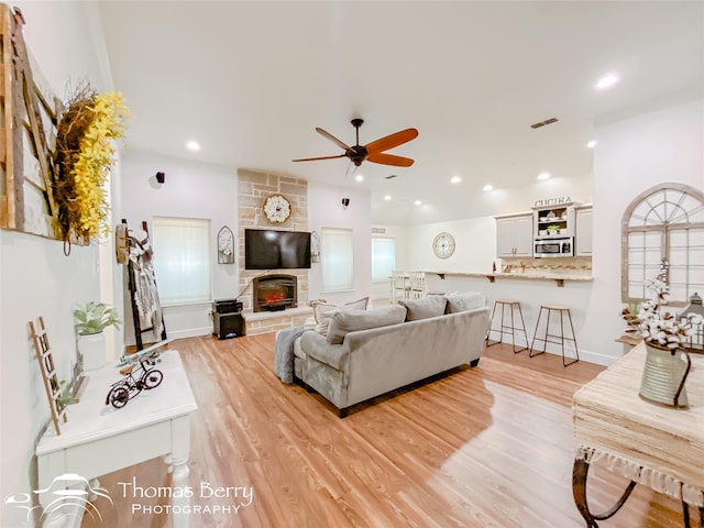 living room featuring a stone fireplace, light hardwood / wood-style floors, and ceiling fan