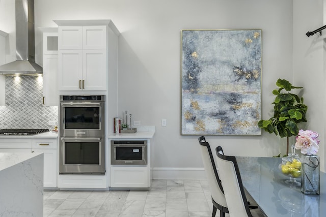 kitchen featuring white cabinets, appliances with stainless steel finishes, wall chimney exhaust hood, and tasteful backsplash