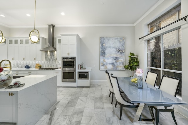 kitchen with white cabinets, decorative backsplash, hanging light fixtures, and wall chimney range hood